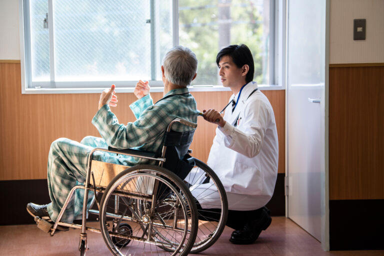 車椅子に乗る高齢男性と医師が会話をしている